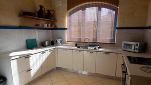 Une cuisine avec des meubles blancs, un évier, une fenêtre avec des stores et un four à micro-ondes.