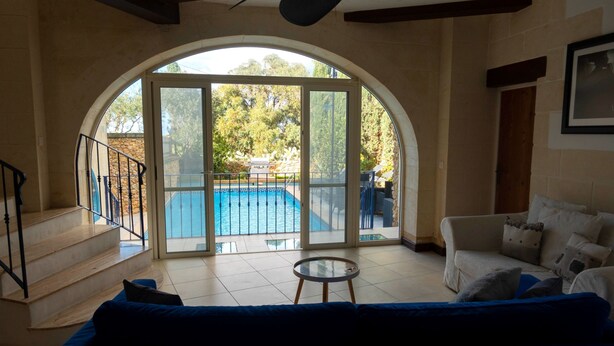 Un vaste espace de vie doté d’une grande porte vitrée en arc de cercle donnant sur une piscine, d’un canapé et d’une petite table.