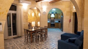 A dining area with a table and chairs, a patterned floor, and an arched doorway leading to a kitchen. - SurWig Vacation Townhouse (Kerċem)