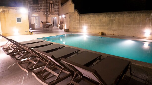 A swimming pool with lounge chairs and a stone building in the background. - SurWig Vacation Townhouse (Kerċem)