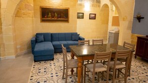 A cozy room with a blue sofa, a wooden dining table with chairs, and a patterned floor. - SurWig Vacation Townhouse (Kerċem)