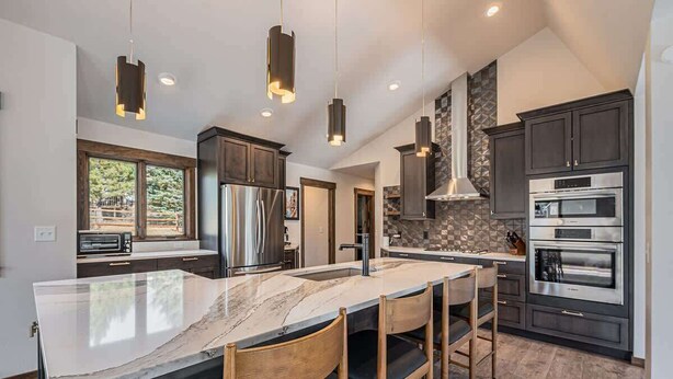 A modern kitchen with a large island, dark cabinets, stainless steel appliances, and pendant lighting.
