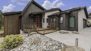 A modern two-story house with a wooden exterior, a red door, and a stone pathway leading to the entrance.