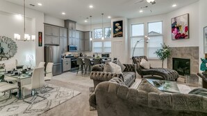 A spacious living room with a fireplace, a dining area with a glass table, and a kitchen with modern appliances. - Home away from home  (Lewisville)