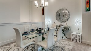 A modern dining room with a glass table, white chairs, a chandelier, and decorative wall art. - Home away from home  (Lewisville)