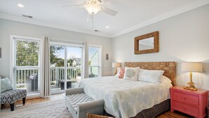 A bedroom with a large bed, a ceiling fan, a nightstand, a bench, and a view of the outdoors through a sliding glass door. - Marsh & River Views, Large Screen Porch, Community Pool & Dock - Crawdads Sing (Folly Beach)