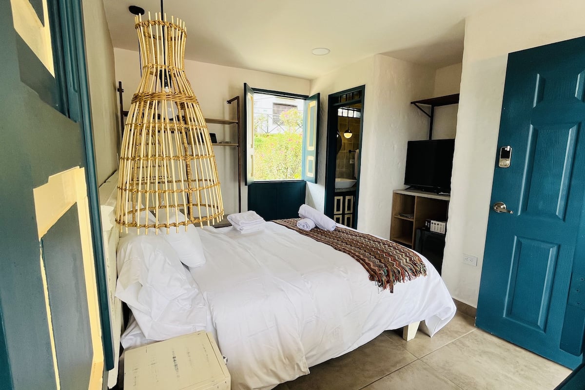 Ein Hotelzimmer mit Bett, Fernseher, Kleiderschrank und einem Fenster mit Blick auf Grünflächen.