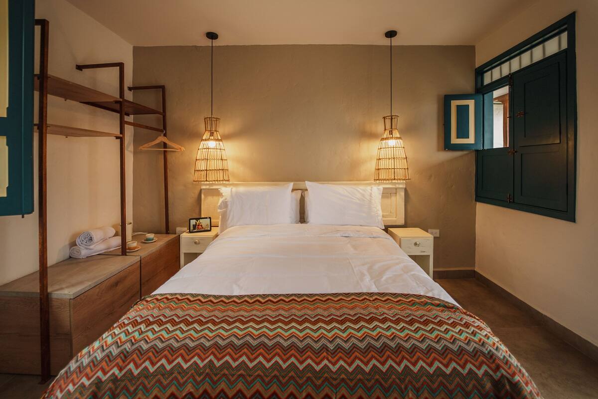Ein Schlafzimmer mit einem Bett, zwei Nachttischen, einer Hängeleuchte, einem Kleiderschrank und einem Spiegel.