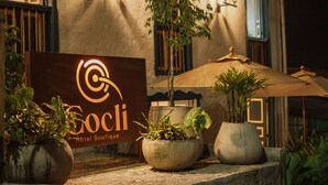 Een hotelschild met een logo en de naam 'Gocli Hotel Boutique'. Er staan potplanten en een grote parasol voor het gebouw.