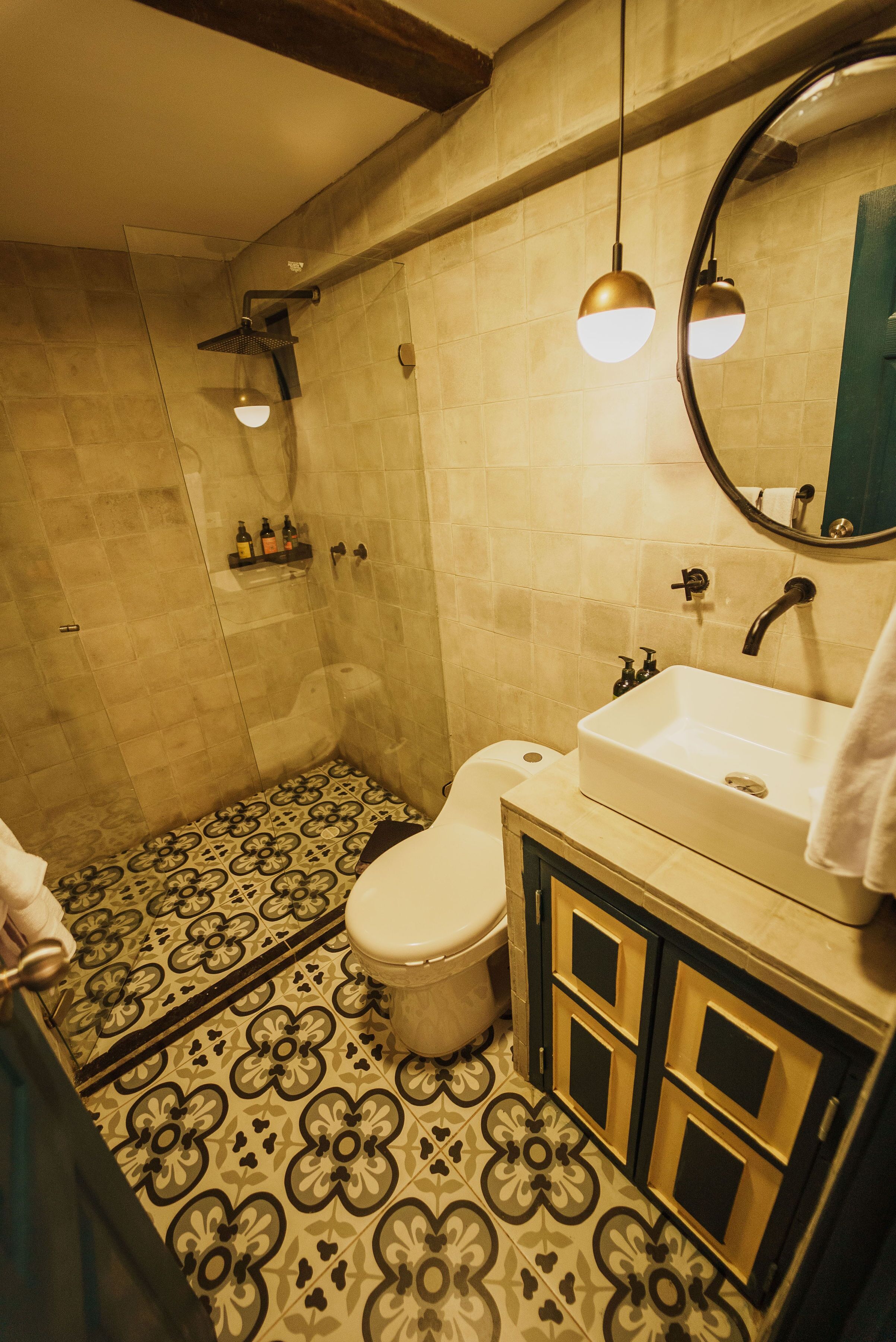 A bathroom with a toilet, sink, and shower. The floor has a patterned tile design.