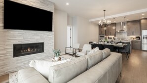A modern living room with a fireplace, a sofa, and a dining area with a kitchen in the background.