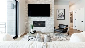 A living room with a fireplace, a flat-screen TV, a leather chair, and a large window.