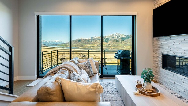 A modern living room with a large sliding glass door leading to a balcony, a leather sofa, a fireplace, and a flat-screen TV.