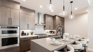 A modern kitchen with stainless steel appliances, a central island with bar stools, and pendant lighting.