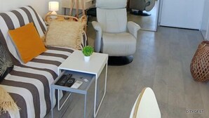 Ein modernes Wohnzimmer mit einem gestreiften Sofa, einem kleinen Beistelltisch mit einer Pflanze, einer Stehlampe und einem grauen Sessel.
