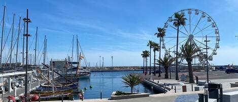 Un port esportiu amb vaixells, una noria i un cel blau clar.