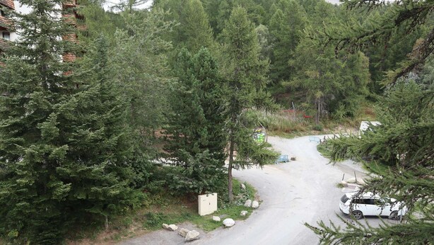 Une route sinueuse traverse une zone boisée, et une voiture blanche est garée sur le bord.