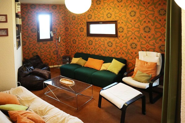 A living room with a green sofa, a white armchair, a glass coffee table, and a brown leather bean bag.