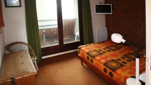 Une chambre à coucher comprenant un lit, un bureau, une chaise, un téléviseur et une fenêtre avec des rideaux.