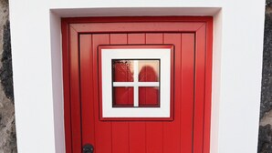 Una puerta roja con una ventana, un felpudo con la palabra “HOME” y un muro de piedra.