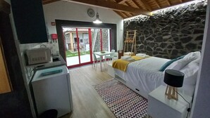 Un dormitorio con cama, mesita de noche, lámpara y pared de piedra. También hay un escritorio con silla y ventana.