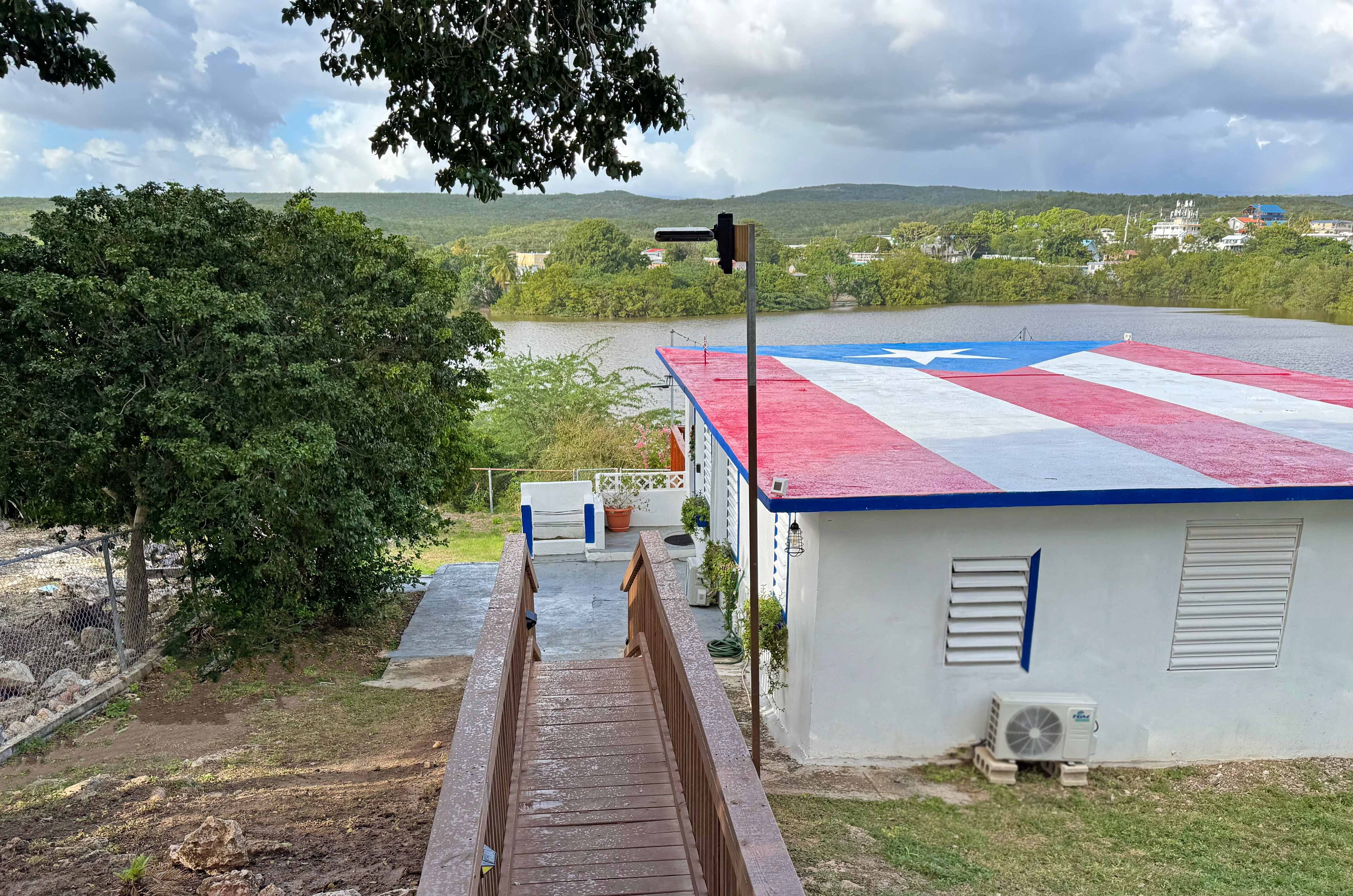 A building with a red, white, and blue roof, a small outdoor area with a wooden deck, and a view of a lake and hills in the background.