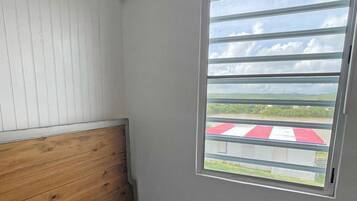 A room with a wooden headboard, a single bed with blue bedding, and a window with a view of a red and white checkered area outside.