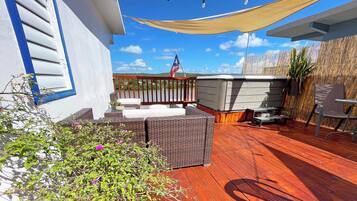 A wooden deck with wicker furniture, a patio umbrella, and a view of a mountain range.
