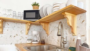 A kitchen with a stainless steel sink, wooden shelves, a microwave, and a hexagonal tile backsplash. - Palmeras Beach Apartments (Guanica)
