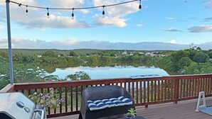 A deck with a grill, a cushioned seating area, and a view of a lake and distant hills. - Palmeras Beach Apartments (Guanica)