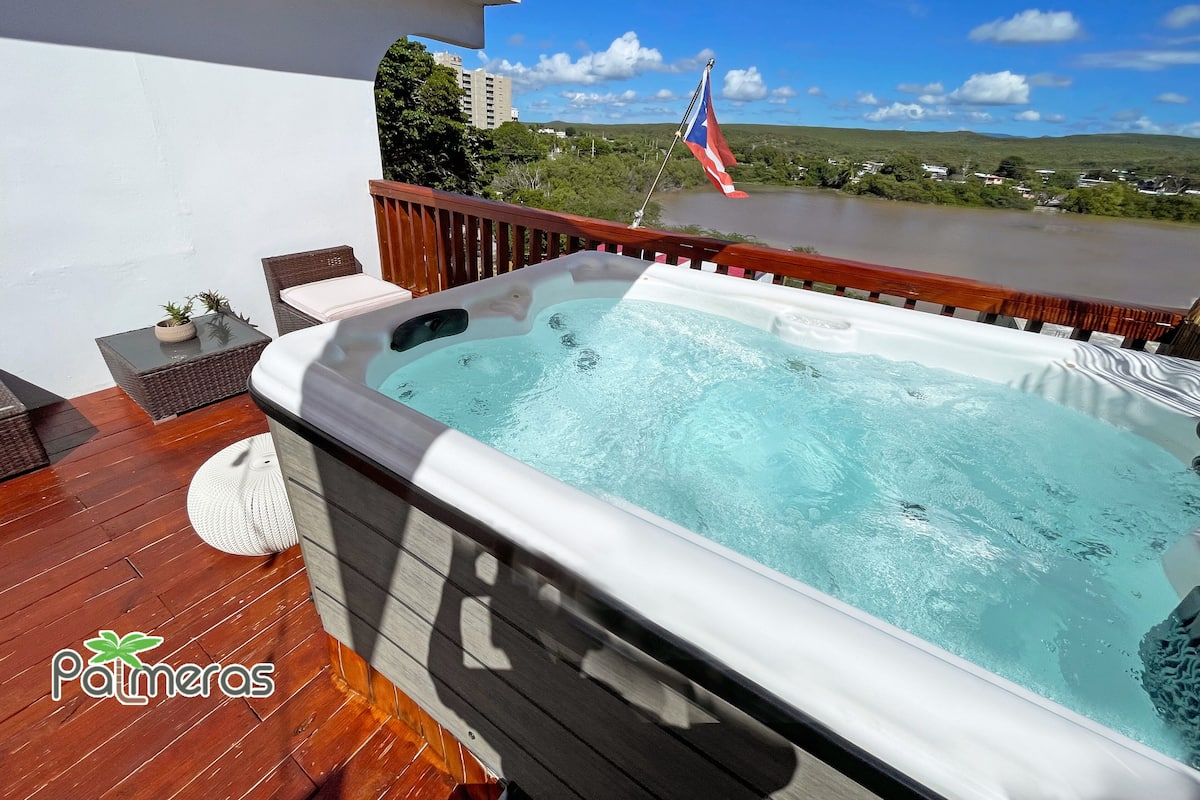 Un bain à remous sur une terrasse en bois, avec vue sur une rivière et des collines.