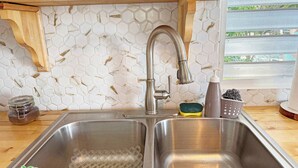 A kitchen with a stainless steel sink, a wooden shelf above, and a hexagonal tile backsplash. - Palmeras Beach Apartments (Guanica)