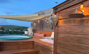 A wooden deck with a hot tub, a hammock, and a view of a town and hills. - Palmeras Beach Apartments (Guanica)