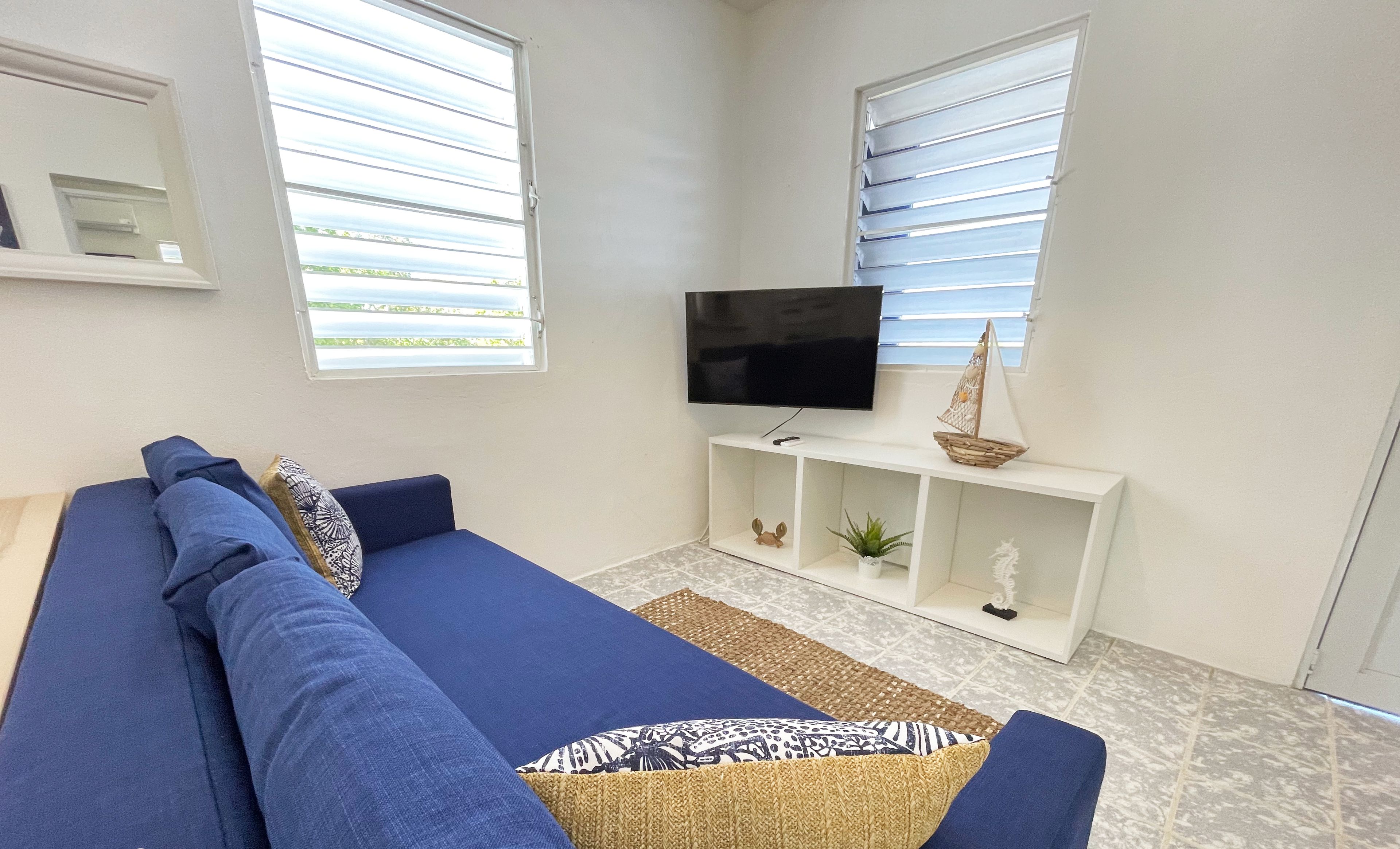 Un salon avec un canapé bleu, un téléviseur et une console blanche agrémentée d’objets décoratifs.