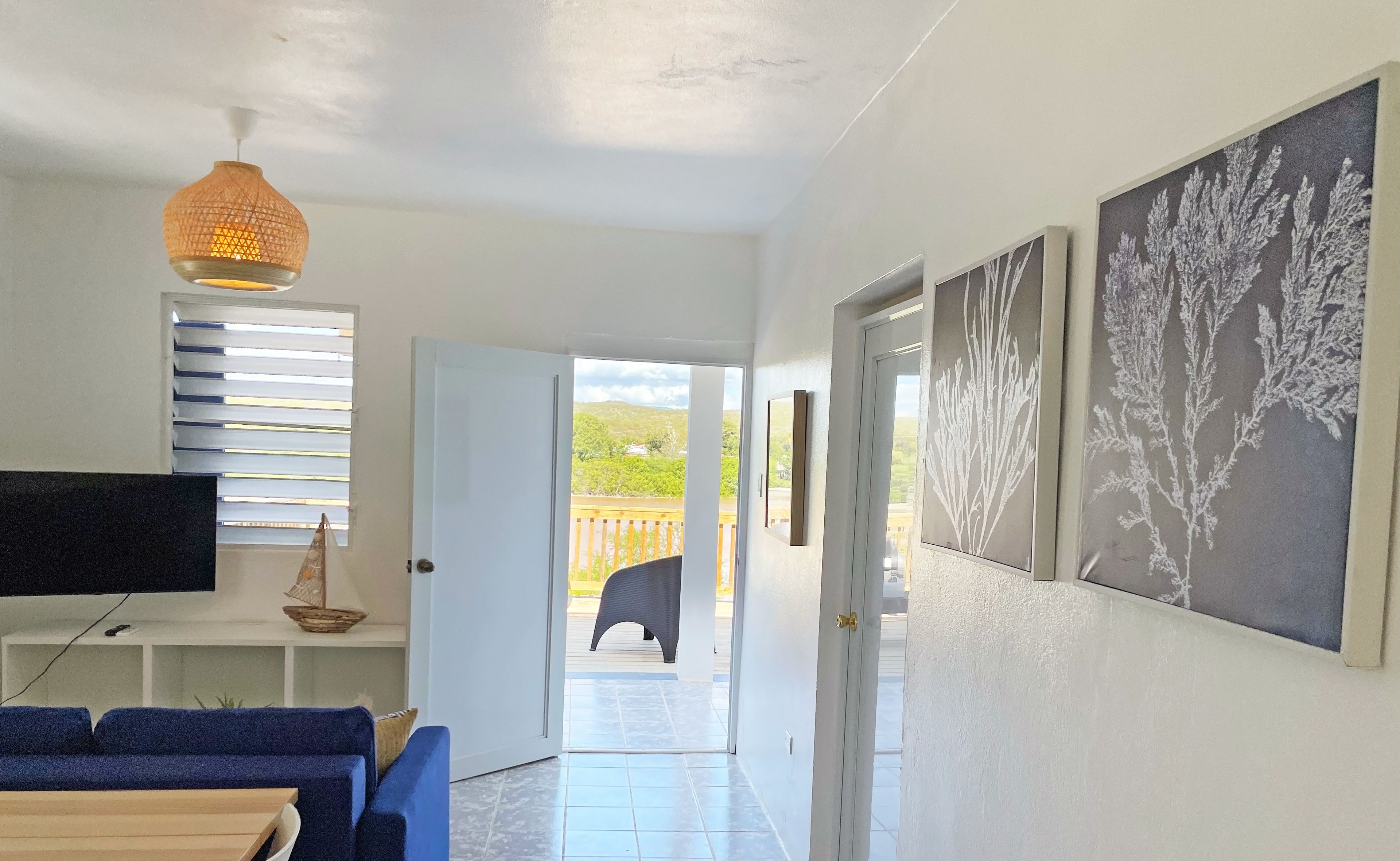 A hallway with a TV, a wooden table, blue chairs, and artwork on the walls.