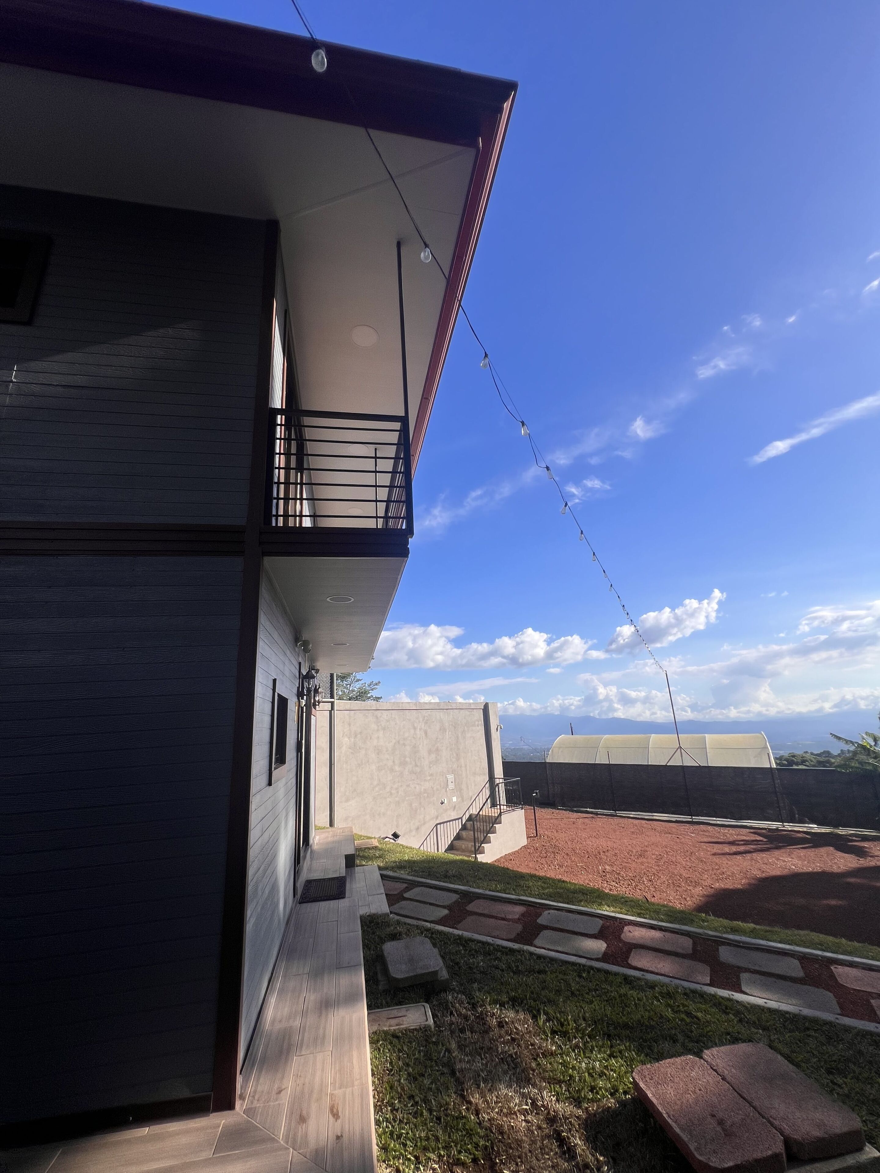Un edificio moderno con balcón, cielo despejado y una vista distante del paisaje.