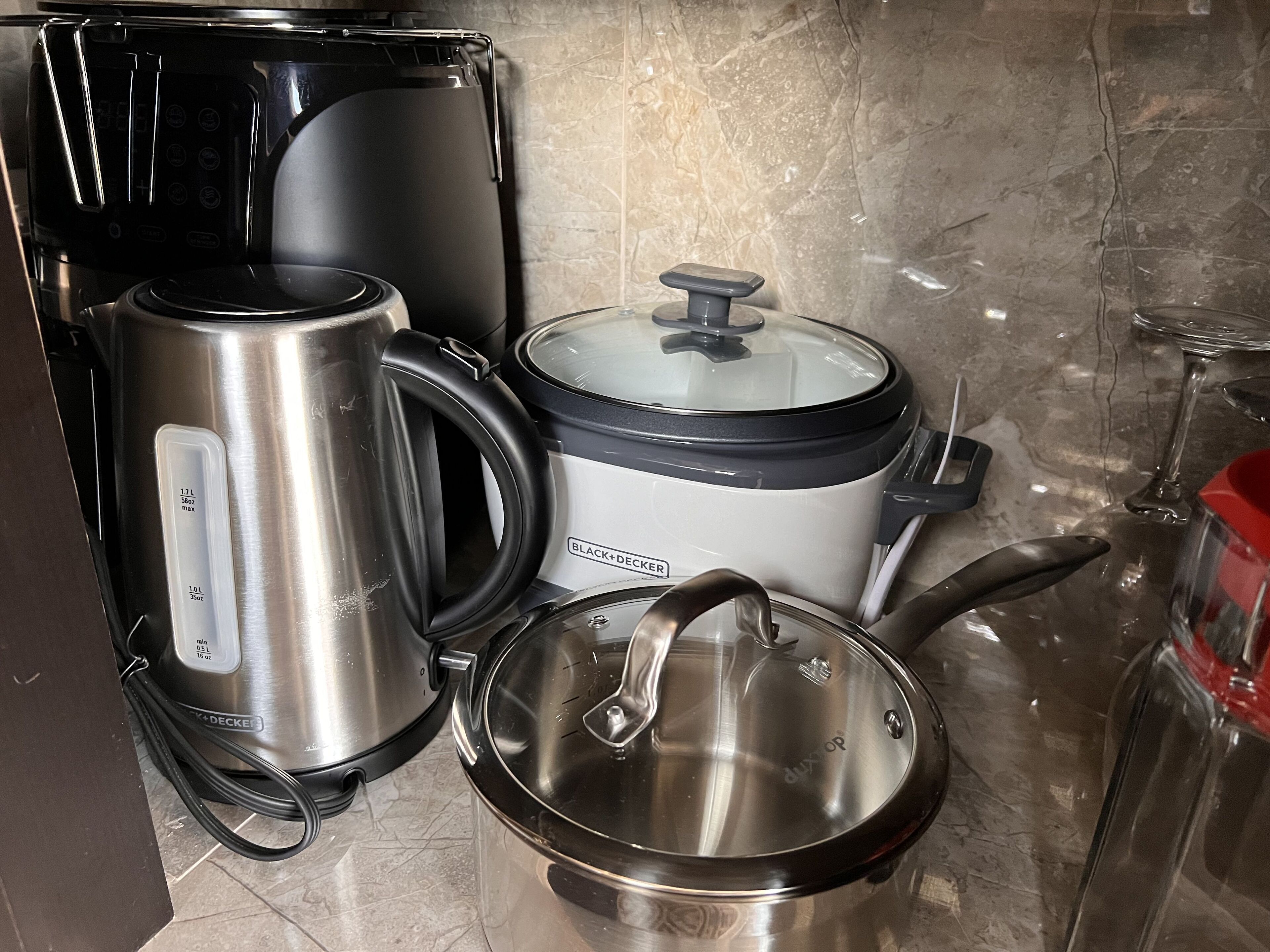 Una cocina con cafetera, olla de cocción lenta y una olla en la estufa.