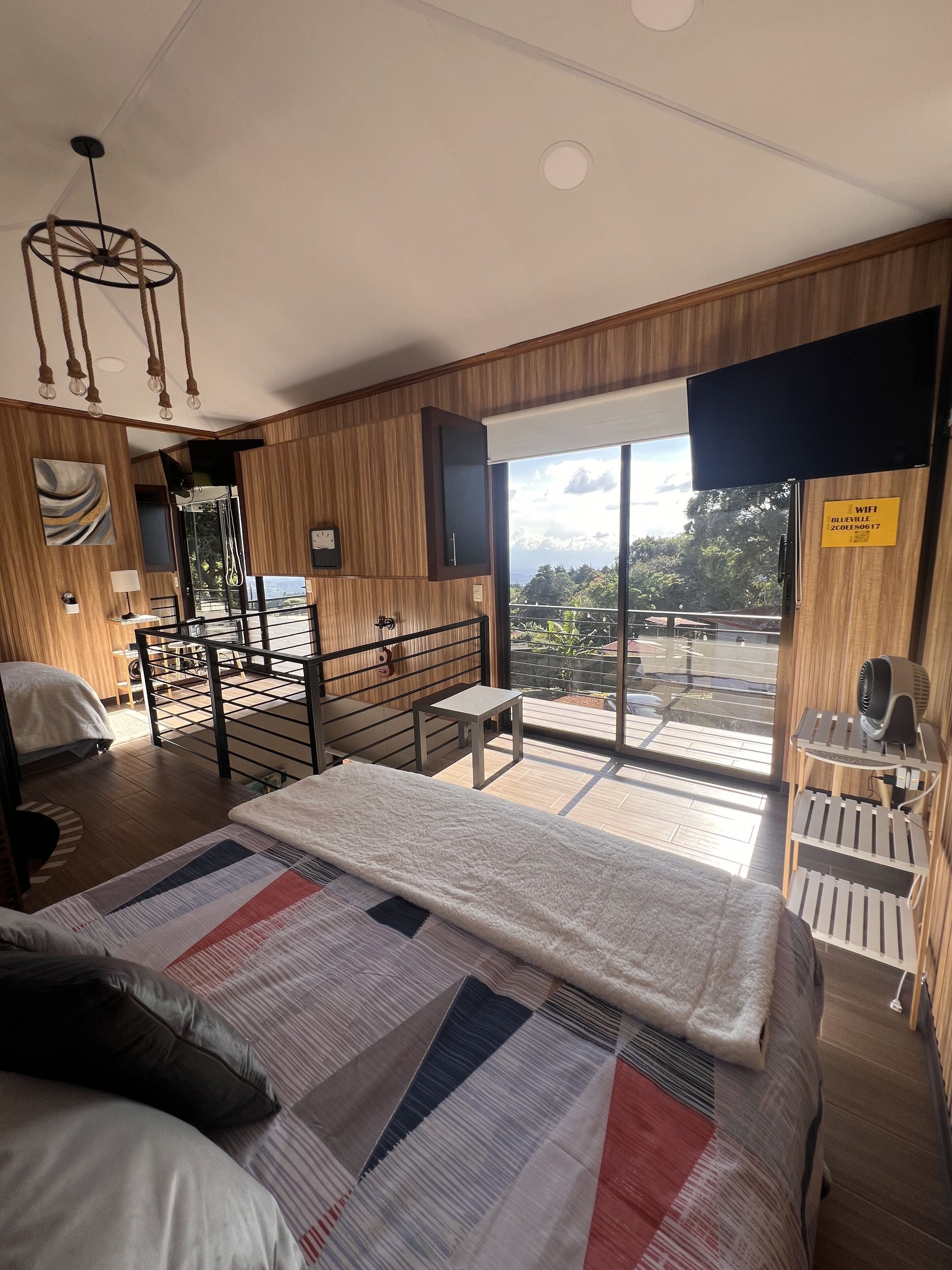 A modern hotel room with a large bed, a balcony with a view, a desk, and a seating area.