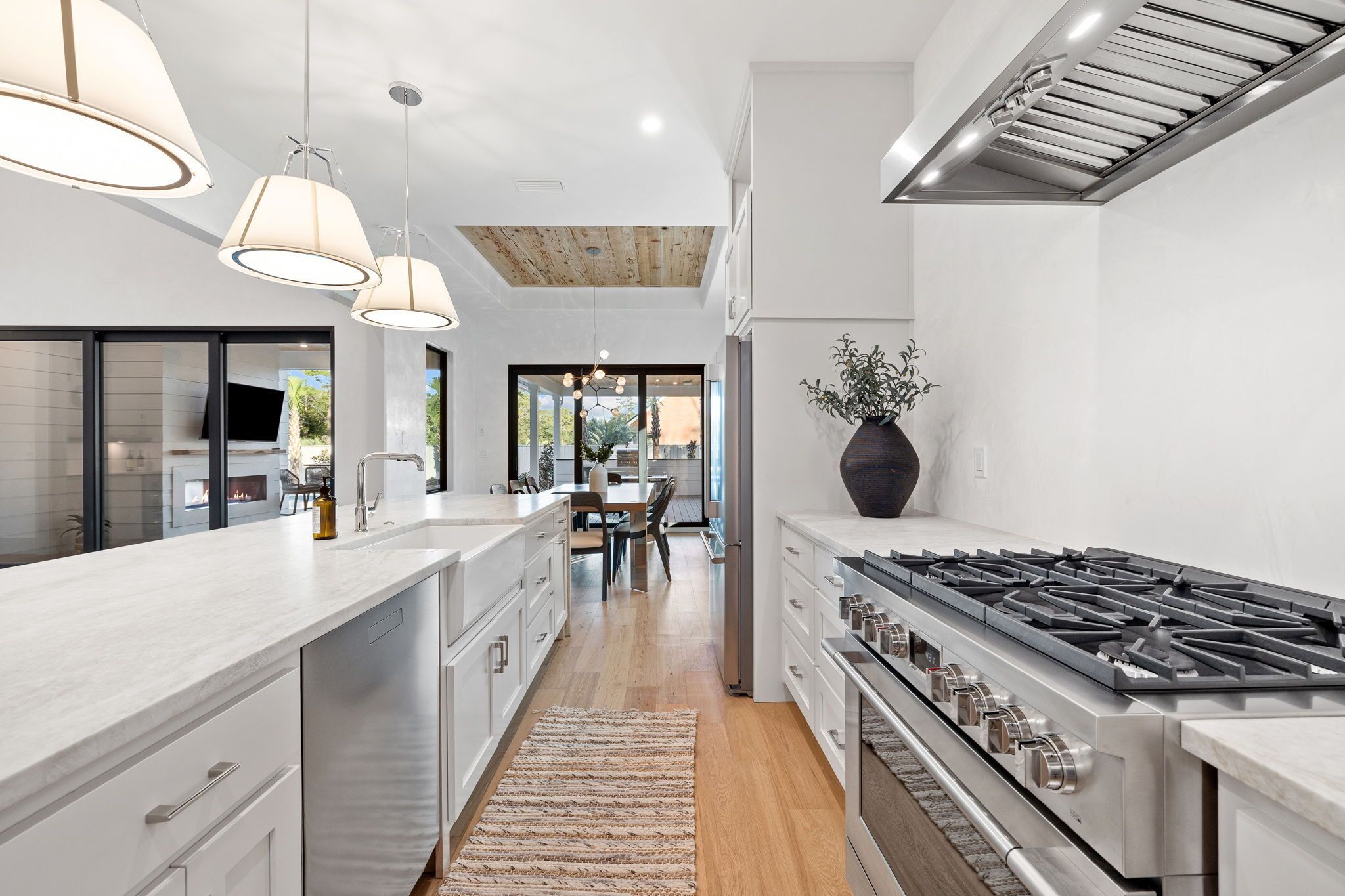 A modern kitchen with a central island, stainless steel appliances, pendant lighting, and a view to a dining area.
