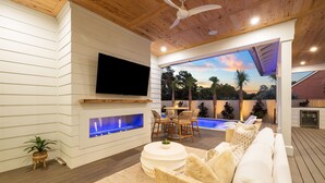 A modern outdoor living area with a wooden ceiling, a flat-screen TV mounted on the wall, a built-in fireplace, a pool table, and comfortable seating. - Private Heated Pool, Single-Level Home, Golf Cart (Inlet Beach)