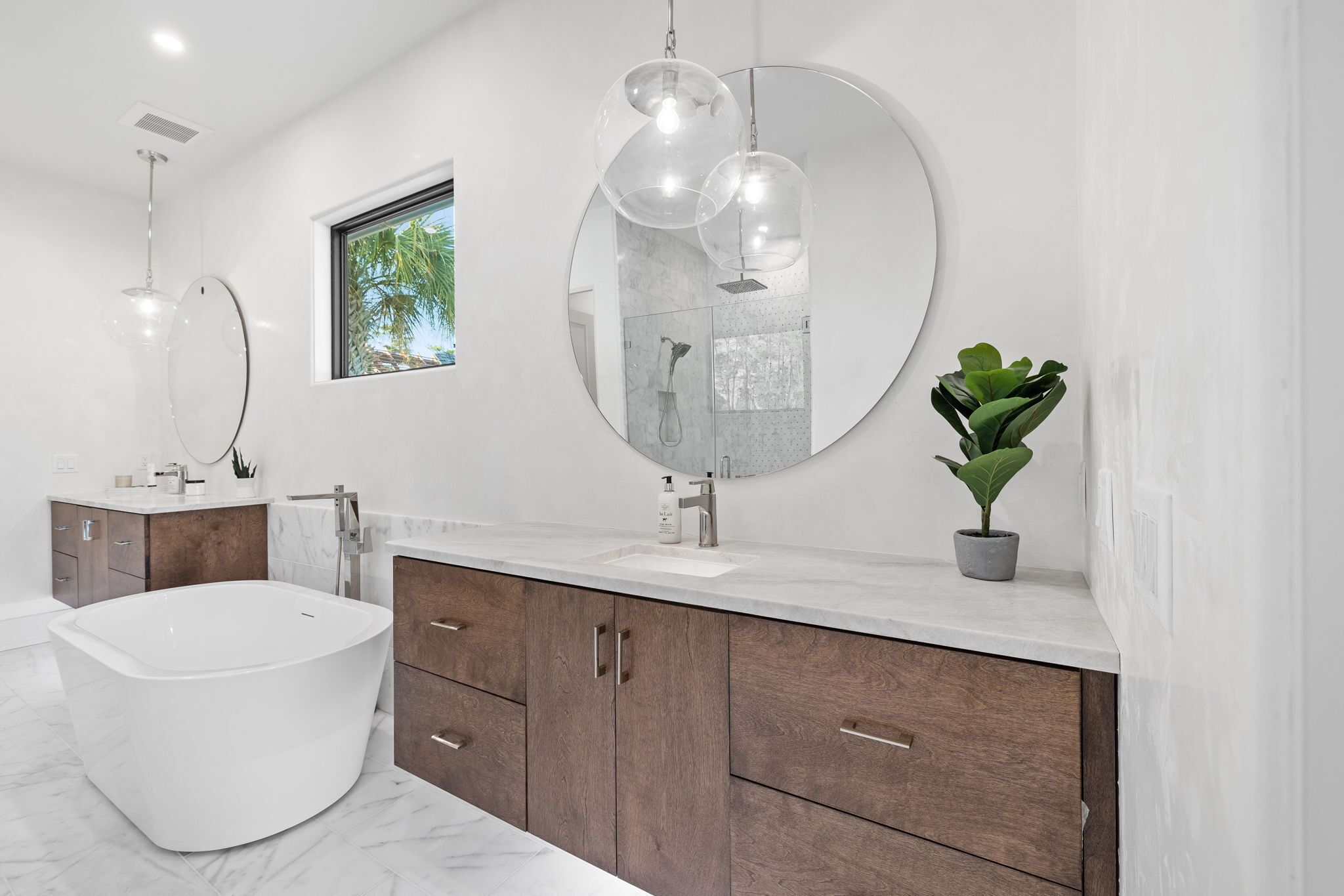 A modern bathroom with a freestanding bathtub, a large round mirror, and a potted plant.