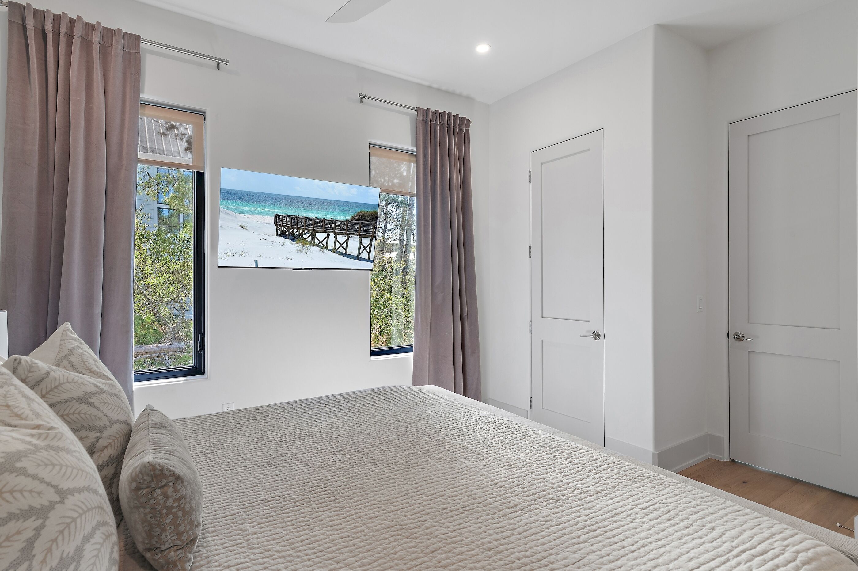 Ein Schlafzimmer mit einem großen Bett, zwei Vorhängen, einer Tür und Blick auf Strand und Steg.