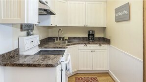 A compact kitchen with white cabinetry, a granite countertop, a coffee maker, and a sign that says "Eat. Sleep. Play." - Northern Michigan gem in a beautiful beach town. (Frankfort)