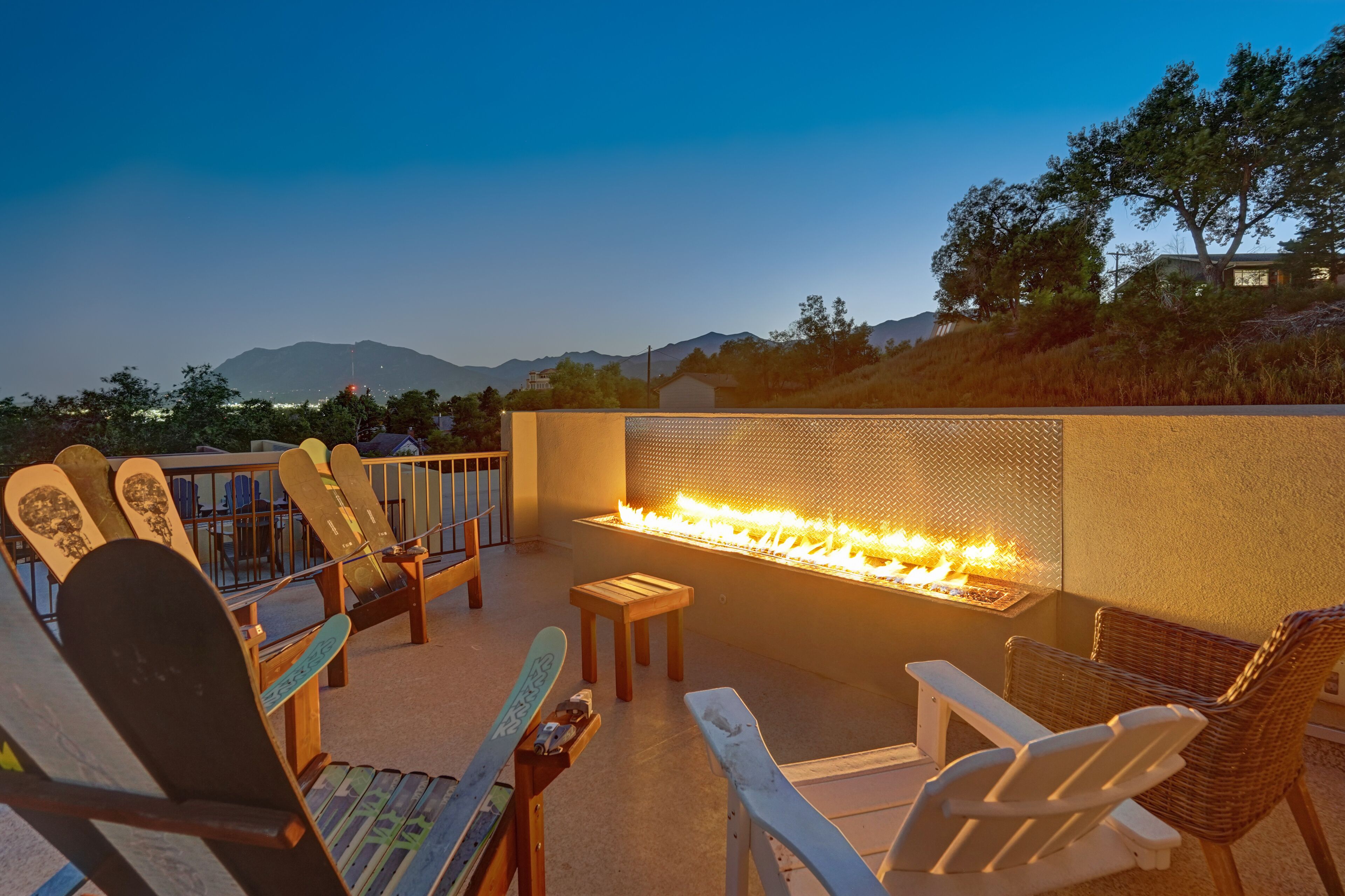 A rooftop patio with a fire feature, seating, and a view of the mountains.