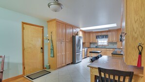 A kitchen with wooden cabinets, a refrigerator, a dining table with chairs, and a window with curtains. - Large Home w/ Deck & Grill ~ 9 Mi to Virginia Tech (Christiansburg)