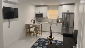 Una cocina moderna con armarios blancos, un refrigerador de acero inoxidable, un microondas y un televisor de pantalla plana montado en la pared.