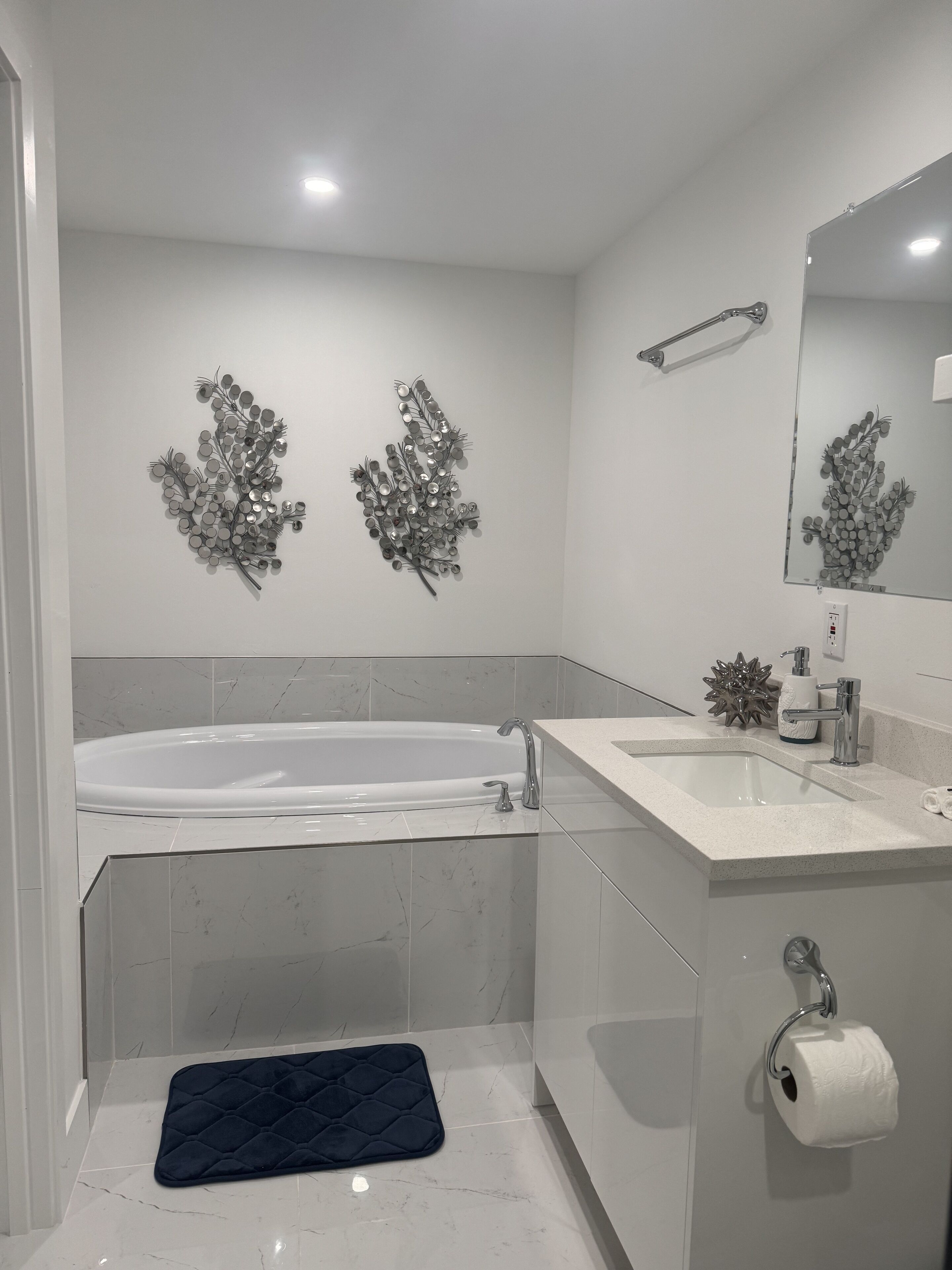 A modern bathroom with a bathtub, a sink, and a toilet. There are decorative wall pieces and a mirror above the sink.