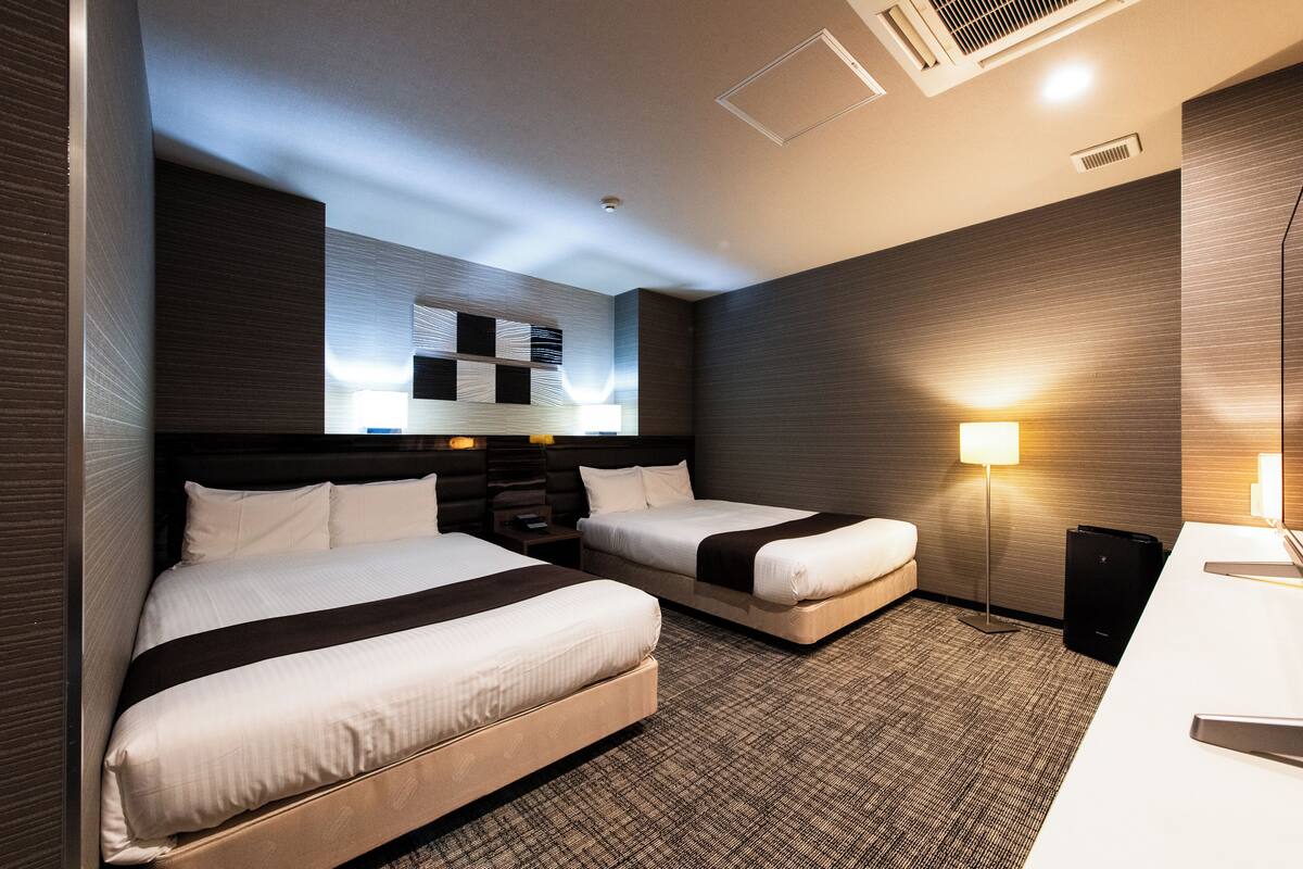 A hotel room with two beds, a desk, a lamp, and a wall-mounted artwork.