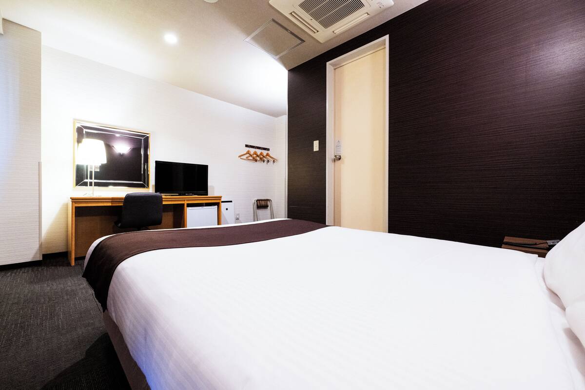 A hotel room with a large bed, a desk with a computer, a chair, a mirror, and a wardrobe.