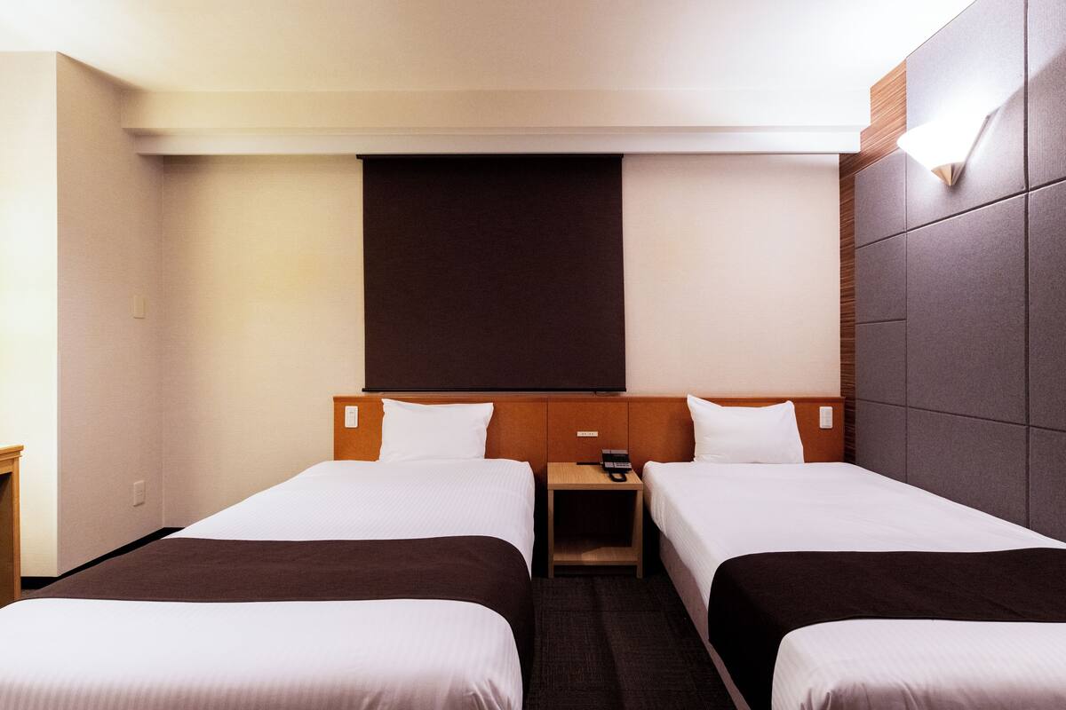 A hotel room with two beds, a wooden headboard, a small bedside table with a phone, and a large wall-mounted TV.